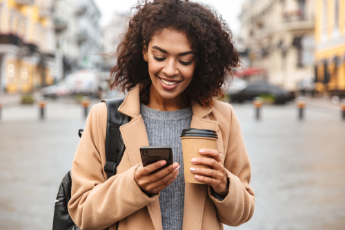 A woman holding a coffee and smiling while looking at her phone