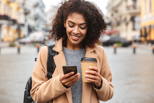 Woman on street with coffee and looking at her phone