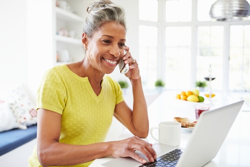 Woman using a laptop and talking on the phone in her kitchen